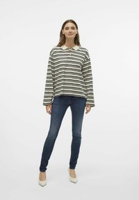 Skrāpjots garās piedurknes polo krekls krēmkrāsā un melnā krāsā ar apkakli un pogu detaļām, apvienots ar tumši zilām šaurām džinsiem un norādītām baltām kurpēm.