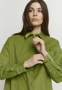 Grøn kordfløjel button-up skjorte med krave, der har en forlommes og knapmanchetter. Tekstureret stof med et ribbet mønster.