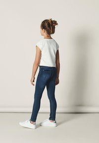 Blue denim skinny jeans with a high waist, paired with a white short-sleeve cropped t-shirt and white sneakers with silver accents.