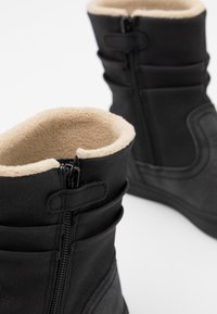 Botas negras con un acabado texturizado, que cuentan con un forro de felpa beige, cierres de doble cremallera y cuellos suaves acolchados para mayor comodidad.