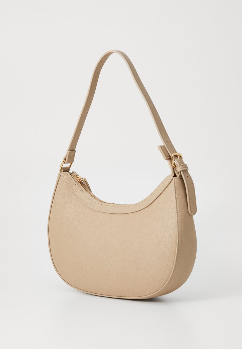 Sac à main en cuir beige avec une forme arrondie, une seule bandoulière et des accents en métal doré ; il dispose d'une ouverture zippée sur le dessus.