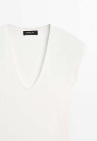 White sleeveless top with a deep V-neck and a black label reading Massimo Dutti sewn inside the neckline.
