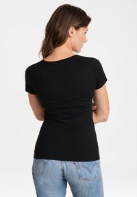 Camiseta negra de manga corta con escote redondo, diseño ajustado y textura suave, combinada con jeans de color azul claro.