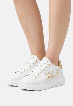Adidași albaștri din piele cu accente aurii și logo, având vârful rotund, șireturi și o talpă groasă. Proiectați pentru purtare casual.