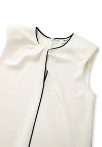 Mouwloze blouse in crème stof met een zwarte bies. Heeft een zachte drape en een sleutelgat-sluiting aan de achterkant met een kleine knoop.