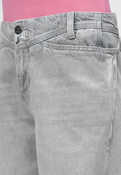 Γκρι τζιν από τζιν ύφασμα με κλασικό σχεδιασμό πέντε τσεπών, μεταλλικά στοιχεία ασημί απόχρωσης και διακριτική ξεθωριασμένη υφή. Διαθέτει κούμπωμα με κουμπί και θηλιές για ζώνη.