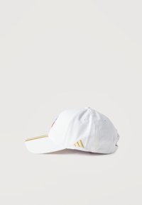 Άσπρο καπέλο μπέιζμπολ με χρυσές ρίγες στο γείσο και χρυσό λογότυπο Adidas στο πλάι, τοποθετημένο επίπεδα σε λευκό φόντο.