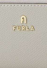 Light gray textured leather wallet with embossed golden "FURLA" logo and stitched accents. Smooth finish, compact rectangular design.