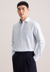 Hellblaues Hemd mit Knopfleiste, das ein dezentes geometrisches Muster aufweist, mit einem Haifischkragen und einer einzelnen Brusttasche, kombiniert mit dunkler Hose.