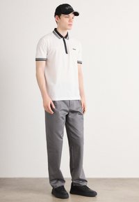 Vit polo skjorta med svart dragkedja och krage accenter, grå byxor och svarta sneakers. Kappen har varumärkets logotyp i vitt.
