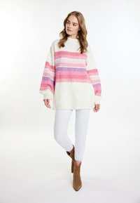 Comoda maglia bianca oversize con pattern a righe rosa, viola e rossi, caratterizzata da un colletto alto e maniche larghe, abbinata a jeans bianchi.