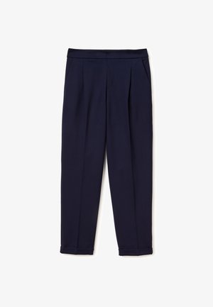 Granatowe, dopasowane spodnie z bocznymi kieszeniami, plisami z przodu i mankietami na nogawkach, ułożone na płasko na białym tle.