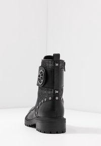 Zwarte enkelboot met een gestructureerde bovenkant, studaccenten, logo-hardware, een chunky hak en een zijrits voor sluiting.