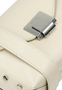 Crème leren handtas met een gepolijste zilveren sluiting, gedetailleerde stiksels en ronde metalen accenten. Gestructureerd ontwerp met een strakke afwerking.