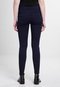 Jean skinny navy avec une texture lisse et une taille haute. Présente des poches arrière et une coupe ajustée, associé à des bottines noires.