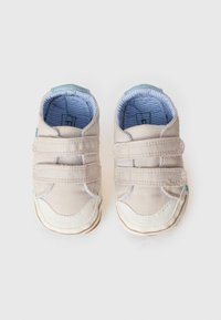 Μπεζ πάνινα παπούτσια βρεφικού τύπου με μπλε λεπτομέρειες, δύο ρυθμιζόμενα λουράκια με αυτοκόλλητο, λευκή καουτσούκ μύτη και ριγέ μπλε εσωτερική επένδυση.