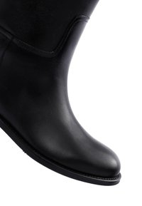 Stivale in pelle nera con texture liscia, punta tondeggiante e dettagli di cucitura minimi. La suola appare piatta e leggermente curvata.
