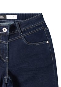 Jeans de mezclilla azul oscuro con bolsillos frontales, cierre de botón plateado, presillas para cinturón y etiqueta dentro de la cinturilla que dice "DENIM".