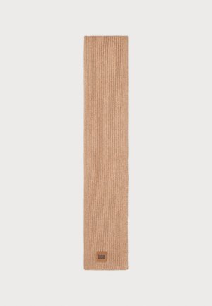 Bufanda de punto acanalado en un cálido color beige, hecha de material suave. Presenta una pequeña etiqueta con el logo marrón de UGG en un extremo.