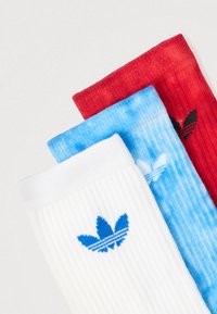 Três pares de meias com nervuras: branco com logótipo azul, tie-dye azul claro com logótipo preto, e vermelho sólido com logótipo preto.