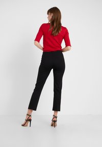 Chemise rouge ajustée à manches courtes, associée à un pantalon noir sur mesure et à des sandales à talons hauts noires à lanières. Design simple et moderne.