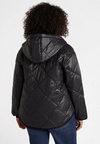 Mustat puffatakki, jossa on huppu, timanttimuotoiltu kuvio, kiiltävä pinta ja elastiset hihansuut. Yhdistetty sinisiin farkkuihin.