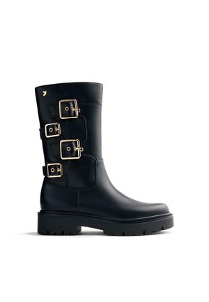 Bottes en cuir noir avec trois accents de boucles dorées, un bout arrondi et une semelle épaisse en caoutchouc noir texturé. Fini lisse.