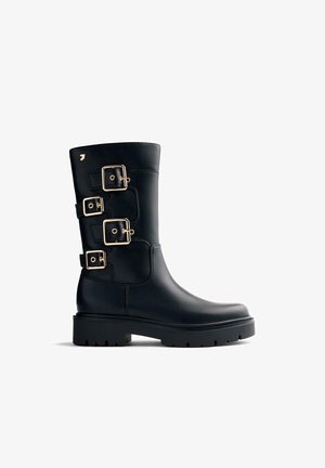 Botas de cuero negro con tres accesorios de hebilla dorada, punta redondeada y una suela gruesa de goma negra texturizada. Acabado suave.
