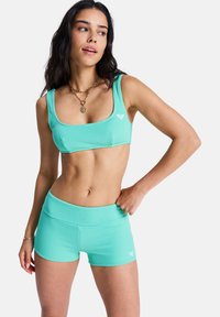 Un brassière de sport côtelée vert menthe et un short assorti, avec une large bande et un petit logo. Texture lisse avec une coupe ajustée.