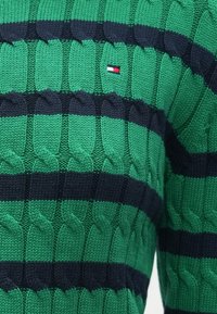 Πουλόβερ πλεκτό με καλώδια, με εναλλασσόμενες οριζόντιες ρίγες σε πράσινο και ναυτικό μπλε, με μικρή λεπτομέρεια λογότυπου σε κόκκινο, λευκό και μπλε στο στήθος.