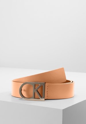 Lysebrunt læderbælte med metalspænde med udskåret "CK" logo, vist sammenrullet på en hvid overflade mod en grå baggrund.