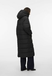 Melna garā pūkainā jaka ar kapuci, kurai ir savilktas horizontālas sadaļas. Savienota ar tumšām izpletu džinsu biksēm un potīšu zābakiem.