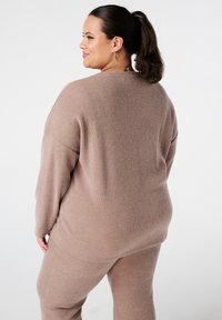 Un pull côtelé marron clair et un pantalon assorti, avec une coupe ample et des fentes latérales pour le confort. Texture douce, design minimal.