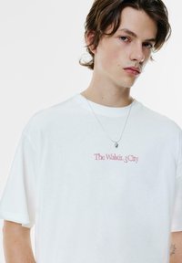 Hvid kortærmet T-shirt med rød tekst "The Walkir. 3 City" på fronten, rund halsudskæring og en afslappet pasform.