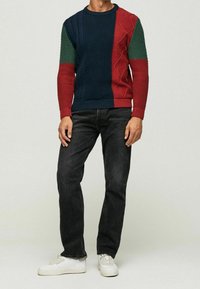 Pullover lavorato a maglia caratterizzato da pannelli blu, verdi e rossi con motivi testurizzati; scollatura rotonda; abbinato a jeans neri e sneakers bianche.