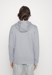 Sudadera gris clara de corte relajado, con capucha ajustable, puños acanalados y una textura suave. Sin patrones ni gráficos visibles.