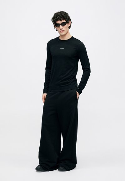 Black long-sleeve shirt with a logo, paired with wide-leg black pants and black sunglasses. Smooth texture, minimal design, and loose fit.