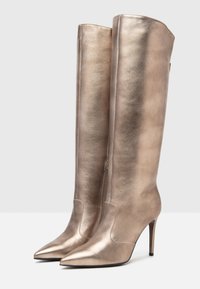 Bottes montantes métalliques dorées avec un bout pointu et un talon aiguille. Fabriquées en matériau lisse avec un design épuré et ajusté, et fermeture éclair sur le côté.