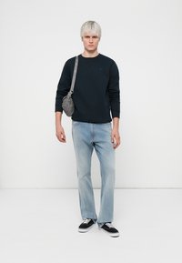 Bluza de marină cu mâneci lungi, blugi drepți de culoare albastru deschis, adidași negri și o geantă crossbody gri cu detalii la curea.
