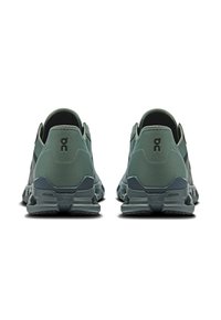 Groene hardloopschoenen met een textuur van gaas aan de bovenkant, een gevoerde hiel en een rubberen zool met een opvallend logo aan de achterkant.