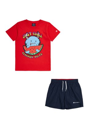 T-shirt rossa in cotone con grafica di un mostro blu e testo "JUST CHILL CHAMPION RULES". Pantaloni corti blu navy con elastico in vita e logo.