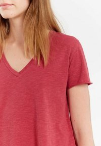 T-shirt rouge à manches courtes en V, fabriqué dans un tissu léger et doux avec une texture subtile et une coupe décontractée.