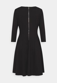 Robe noire longueur genou avec manches longues, corsage ajusté, jupe évasée et fermeture éclair argentée visible courant le long du dos au centre.