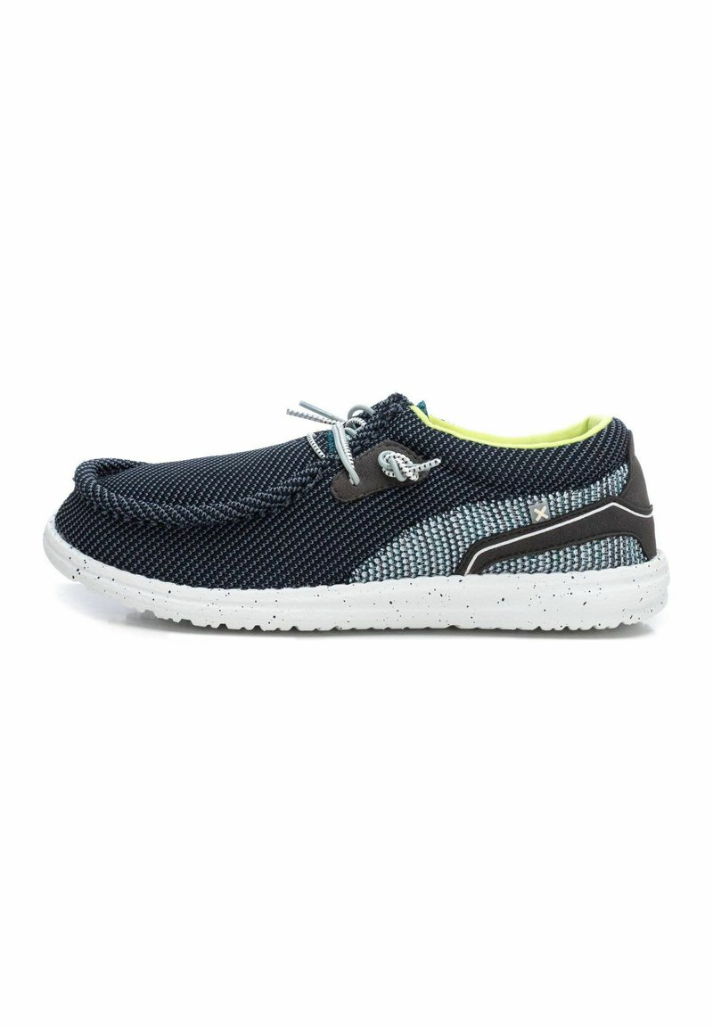 Zapato textil azul marino y gris con suela moteada blanca, puntera redondeada, diseño de cordones y forro interior de color verde brillante.