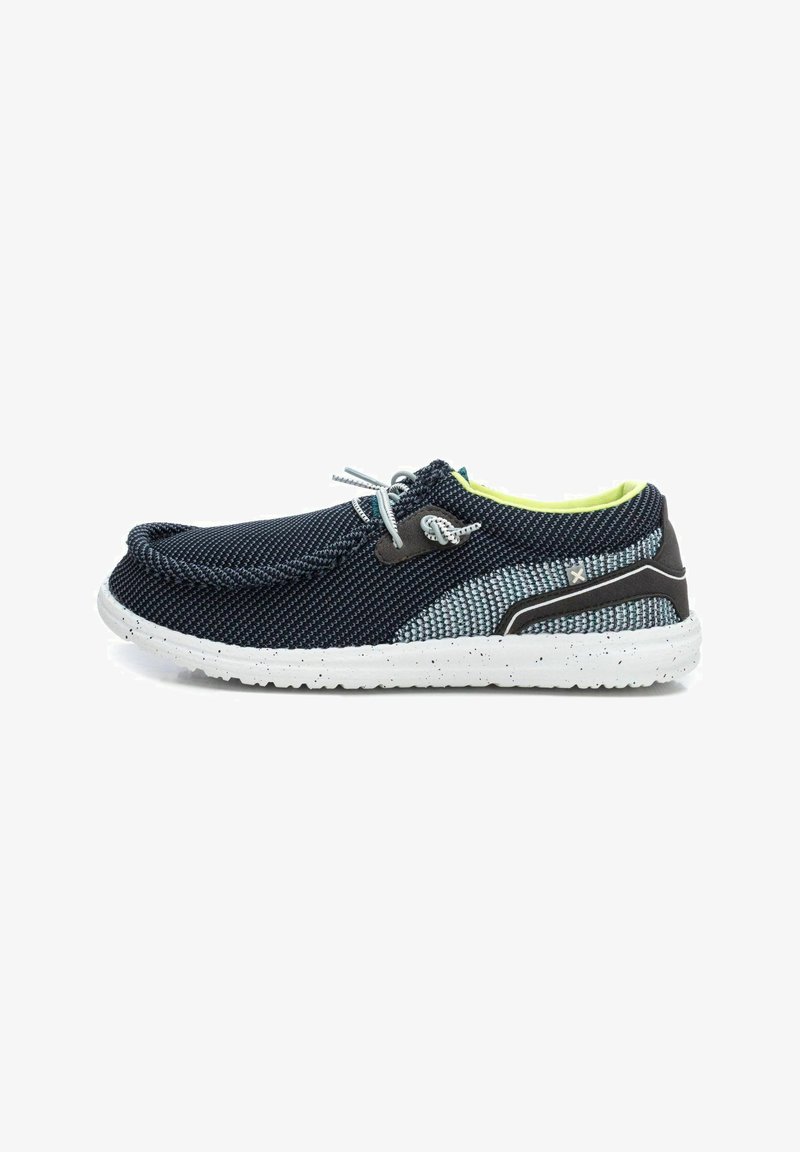 Zapato textil azul marino y gris con suela moteada blanca, puntera redondeada, diseño de cordones y forro interior de color verde brillante.