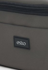 Grijze stoffen tas met een gestructureerde afwerking, voorzien van een zwarte ritssluiting en een rechthoekig zwart label met het woord "estro" in zilver.