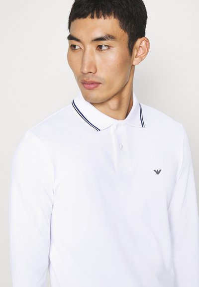 Weißes Langarm-Polohemd mit kontrastierendem navyfarbenem Kragen und einer Knopfleiste mit drei Knöpfen, ausgestattet mit einem kleinen schwarzen Logo auf der Brust.