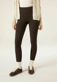 Bruine geribbelde leggings met een hoge tailleband, gecombineerd met donkerbruine sneakers en crème enkelsokken. Gestructureerde stof met een aangesloten ontwerp.