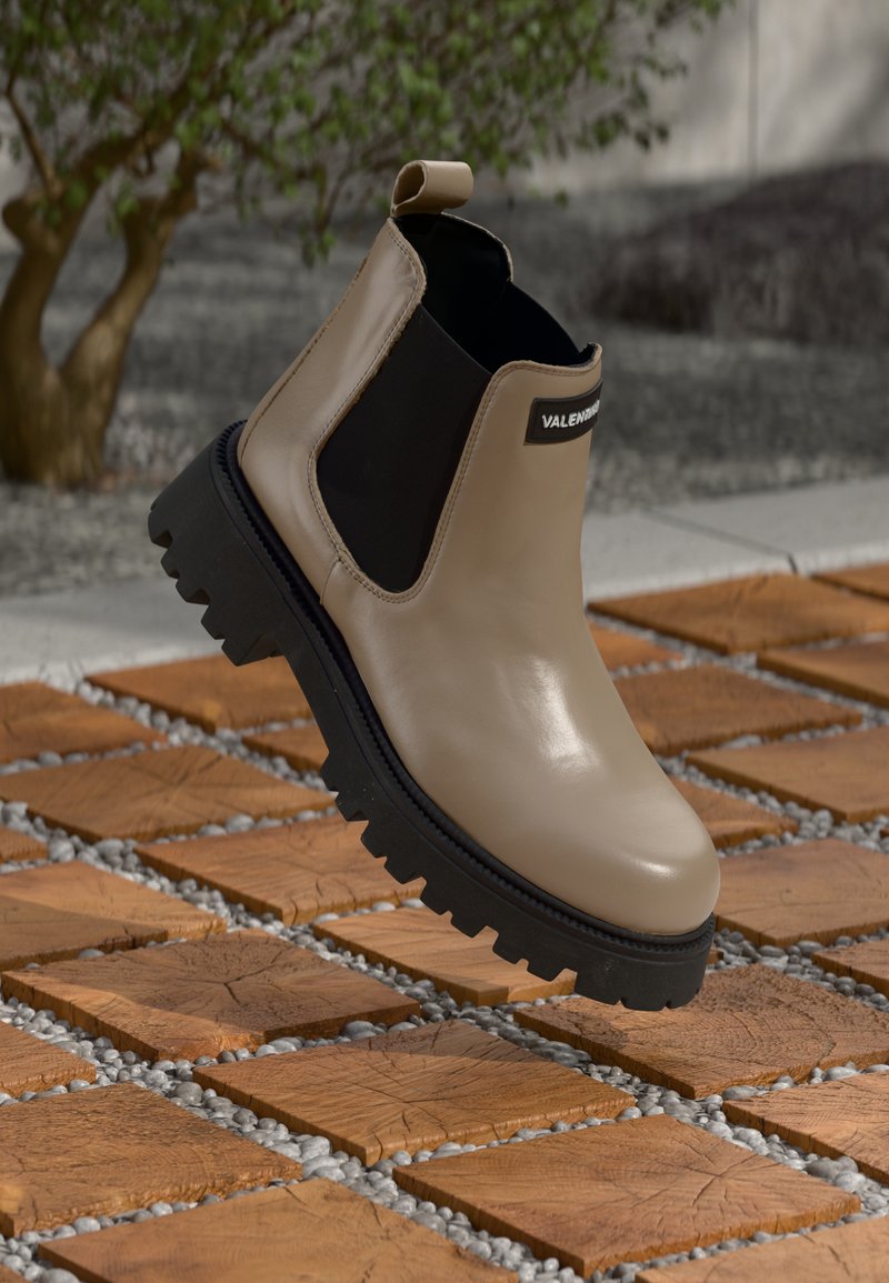Beige lær ankle boot med sorte elastiske sidepaneler og en tykk, robust såle, med en trekkstraps og logoakkent på siden.