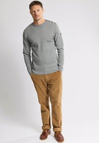 Maglione grigio a maniche lunghe con collo rotondo e quattro bottoni sulle spalle, abbinato a pantaloni in velluto a coste marroni e scarpe stringate marroni.